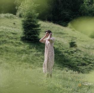 Eine Frau in einem Kleid steht auf einer grünen Wiese in hügeliger Landschaft