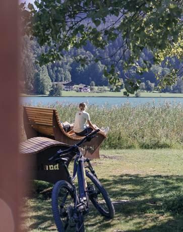 Ein ruhiger Moment am Ufer des Thiersees Eine Frau auf einer Bank am Seeufer, hinter ihr ein Fahrrad.