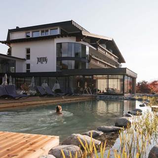 Eine Person schwimmt durch einen natürlichen Außenpool des Juffing Hotel & Spa
