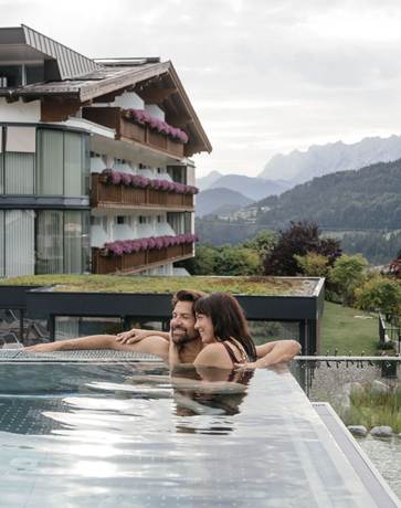 Innige Momente in der Natur Ein Paar kuschelt im Infinity Pool mit Blick auf die umliegenden Berge.