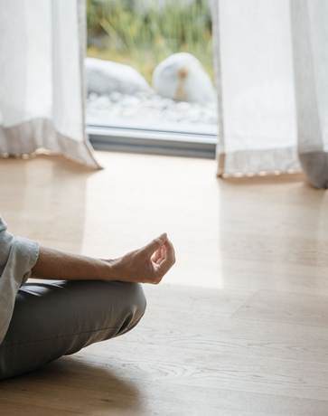 Arm und Bein einer Person die in einer Meditationspose auf dem Boden sitzt.