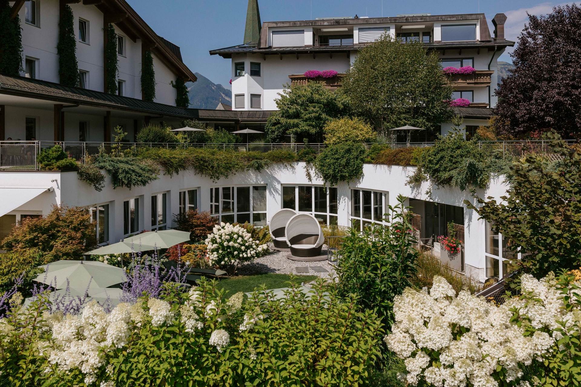 Das Juffing vereint alle Zutaten, die eine gelungene Coolcation ausmachen Garten im Hotel Juffing mit blühenden Blumen, Liegen und Sonnenschrimen.