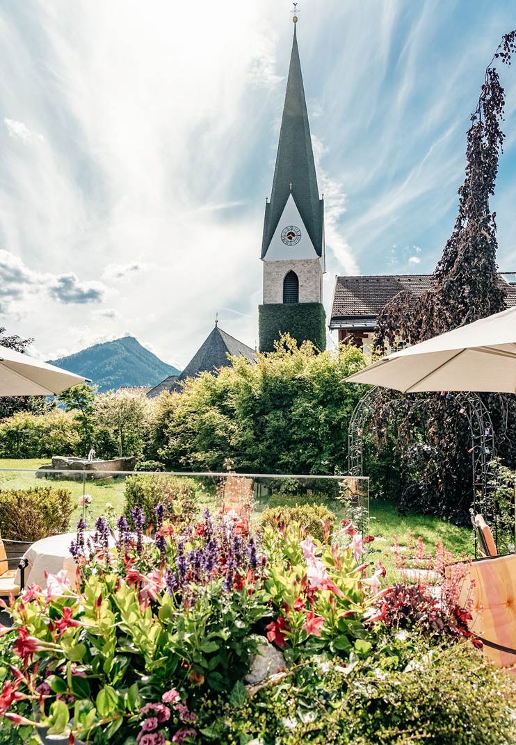 Grüner Garten des Hotels mit vielen Blumen und einen Blick auf den Kirchturm