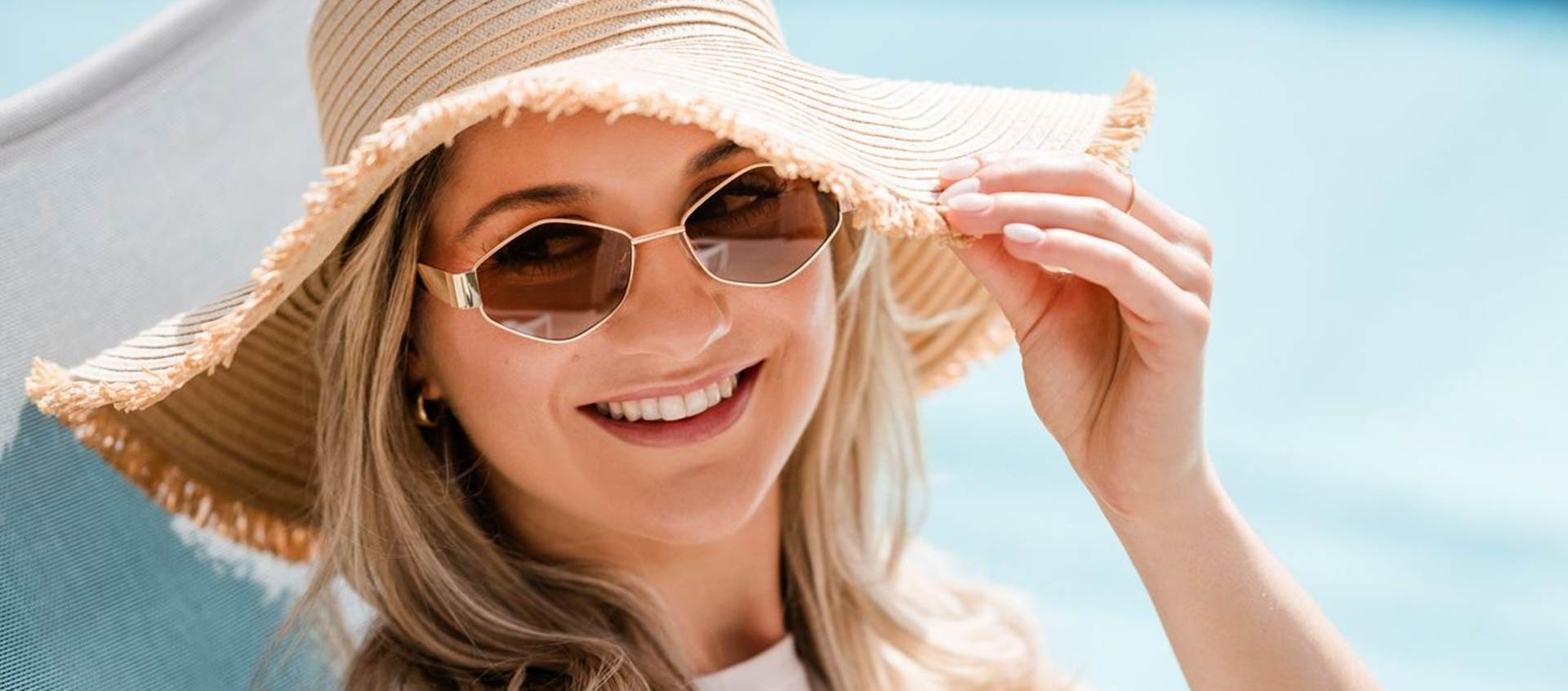 Konsequenter Sonnenschutz – auch im Schatten Lächelnde Frau mit Hut und Sonnenbrille.