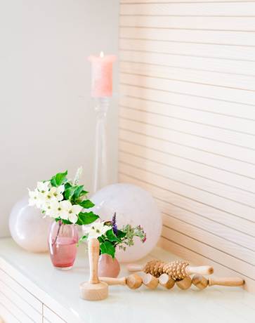 Neben dem spürbaren Wohlfühleffekt hat die Maderotherapie auch handfeste kosmetische Wirkungen Holzinstrumente für Maderotherapie auf einer Ablage mit Blumenvasen uns Kerze.