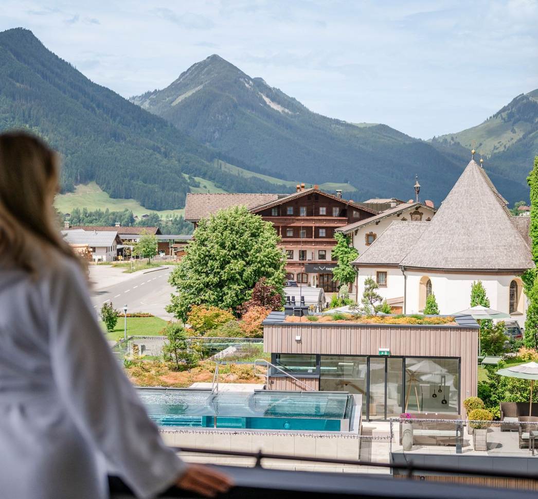 Eine Frau im Bademantel schaut vom Balkon aus auf den Außenpool des Hotel Juffing.