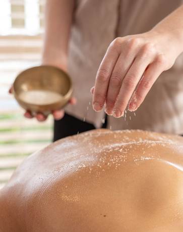Sanftes Peeling gegen aufgestaute Talgproduktion Masseur streut Salz auf den Rücken des Massierten.